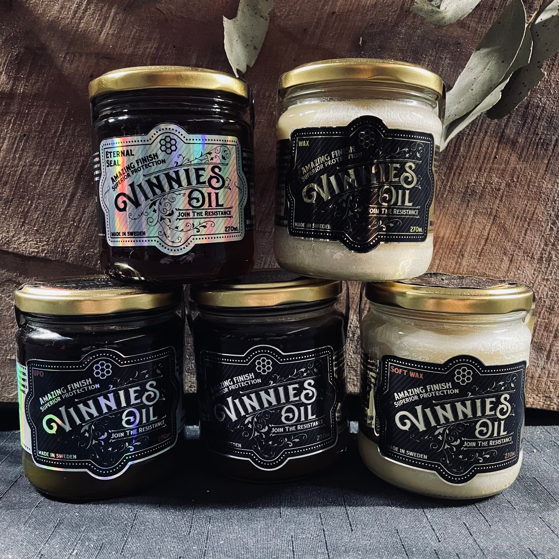 Five jars of Vinnies Oil on a wooden surface with a rustic background.