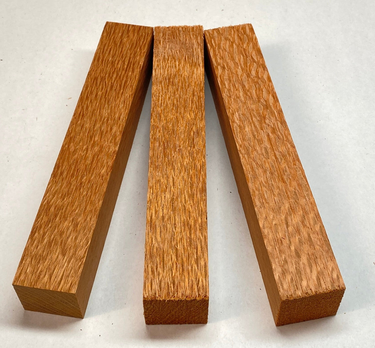 Three rectangular wooden blocks with a warm honey-brown wood grain finish, arranged upright in a row on a light off-white background.