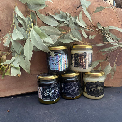 Five jars of 'Vinnie's Oil' with gold lids on a wooden surface with eucalyptus leaves.